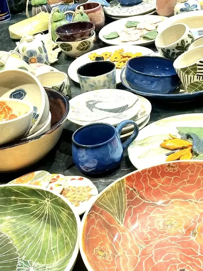 A glimpse of my stall at a pop up, filled with a variety of my handmade ceramics. You can see large floral platters, hand-painted mugs with geometric patterns, and an assortment of bowls, each with its own distinct character and glaze.