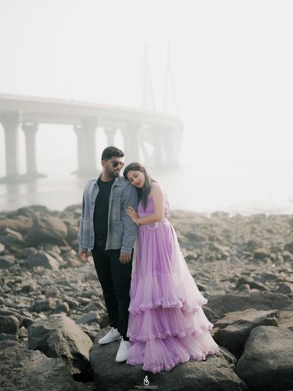 A moody and romantic portrait on a rocky shore, with a misty bridge in the background. This shows how we can use foggy weather to create atmospheric photos.