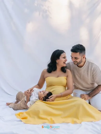 A relaxed family portrait during their outdoor session. The simple white sheet on the grass creates a clean, bright space to focus on their happy interactions as they wait to become a family of four.