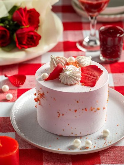 A delicate pink strawberry mini cake decorated with meringue kisses, set against a romantic red and white checkered background.