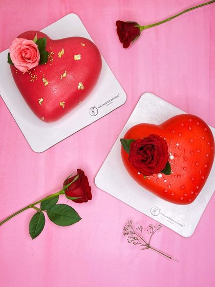 A closer look at two of our romantic heart-shaped cakes. One is a vibrant red with gold leaf, and the other is a soft pink with pearl details, both topped with fresh roses.