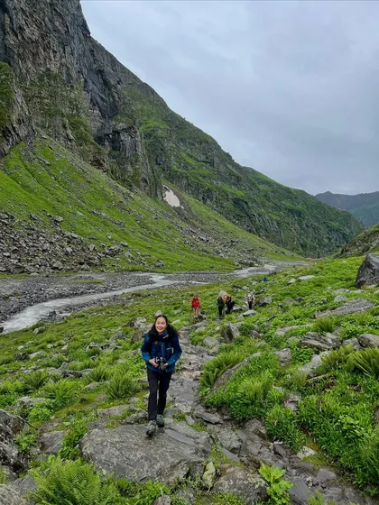 A trekker walking through the vibrant green landscape of the Kullu valley side of Hampta Pass.