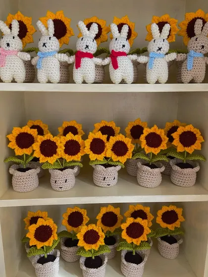 A detailed look at the shelves holding amigurumi bunnies and rows of potted sunflowers for a wholesale order.