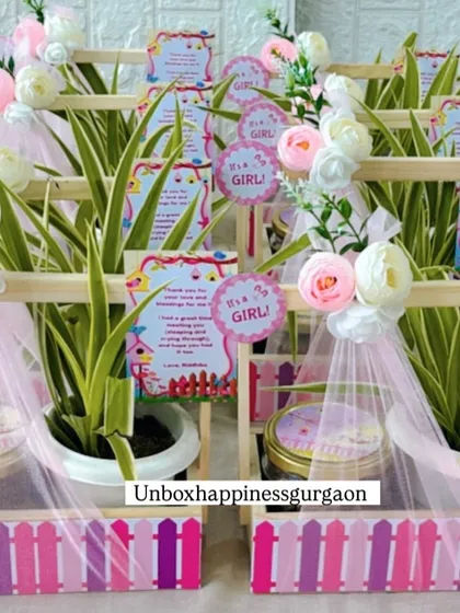 A beautiful display of pink-themed return favors, each containing a lush green plant and a jar of treats.