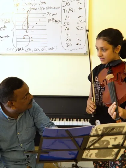 Our lessons combine practical playing with essential music theory. This student is in a violin training session, referencing both sheet music and notes on the whiteboard that explain concepts like solfege hand signs and musical notation.