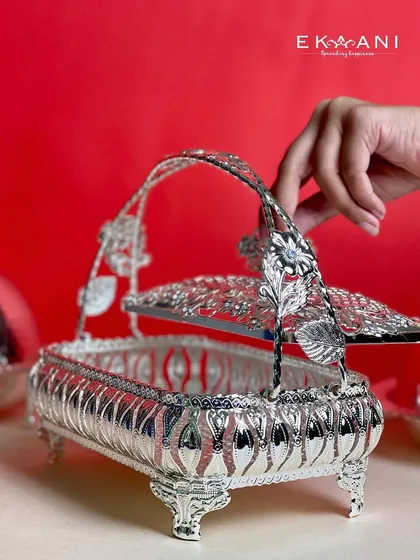 A hand lifts the lid of the ornate silver basket, revealing its utility. It is a piece designed for both grand presentation and practical use during celebrations.