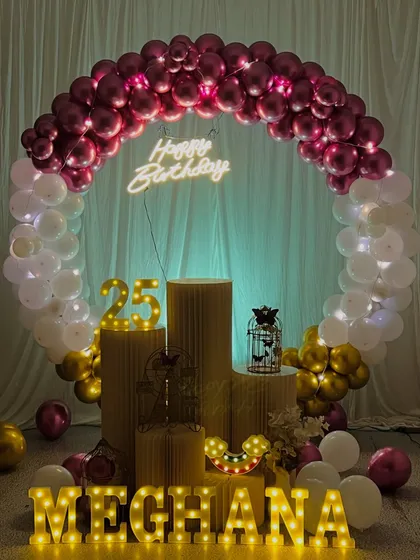 A brightly lit version of the 25th birthday setup for Meghana. This shows how the decoration looks with full lighting, highlighting the chrome balloons and props.