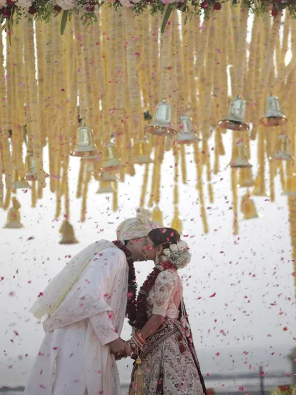 A kiss to seal the promise. This romantic moment is captured under a beautiful floral canopy, with petals showering the couple, marking the beginning of their forever.
