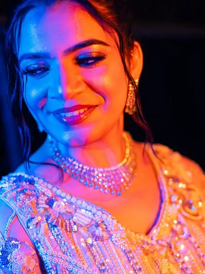 A dramatic, colorful shot of the bride, her glittery eye makeup and diamond necklace shining under the party lights.
