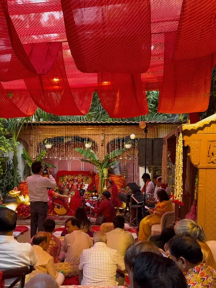 A wide shot of the Mata Ki Chowki setup. Guests are seated facing the beautifully decorated stage, under a ceiling draped with red bandhani fabric, creating a devotional and immersive environment.