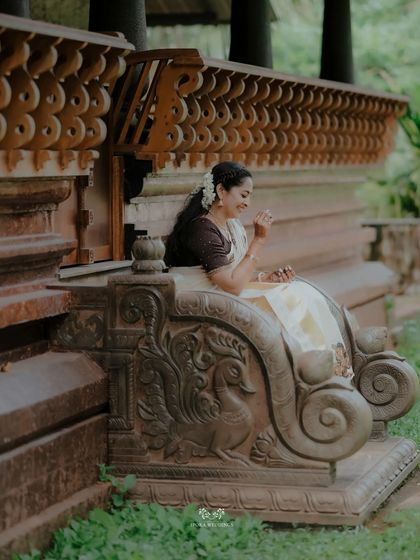 The bride smiling as she sits on a beautifully carved stone bench, a picture of grace and happiness.