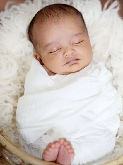 Simple, pure, and timeless. A 24-day-old baby wrapped snugly in white, sleeping peacefully in a soft, fluffy basket.