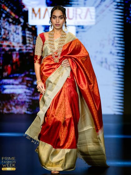 A stunning red and off-white Kanchipuram silk saree, its rich red body and shimmering border making a powerful statement on the runway.