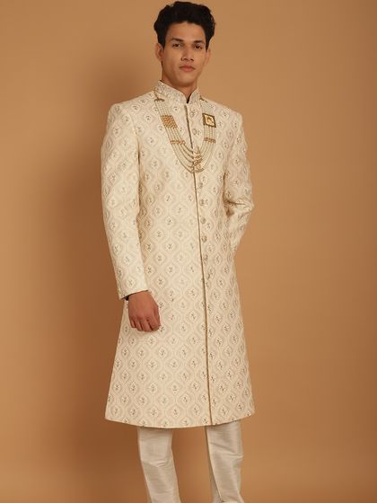 A full-length view of a groom in a classic ivory sherwani, showcasing the regal silhouette and the importance of perfectly coordinated accessories for the complete wedding day look.