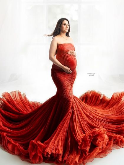 A classic and powerful pose in a strapless red mermaid gown. The ruffled train spreads out beautifully, creating a strong silhouette against the bright, high-key background for a glamorous maternity photo.