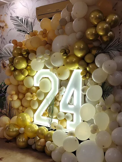 A beautiful wall of balloons in white, cream, and gold, with a large light-up "24" as the centerpiece for a birthday celebration.