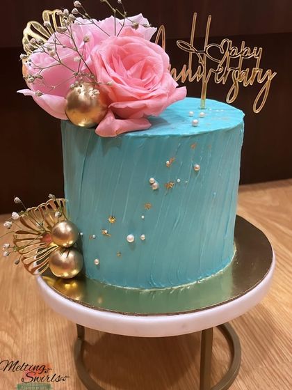 We love creating beautiful buttercream cakes. This one features a textured turquoise finish, adorned with fresh pink roses and gold accents for an anniversary.