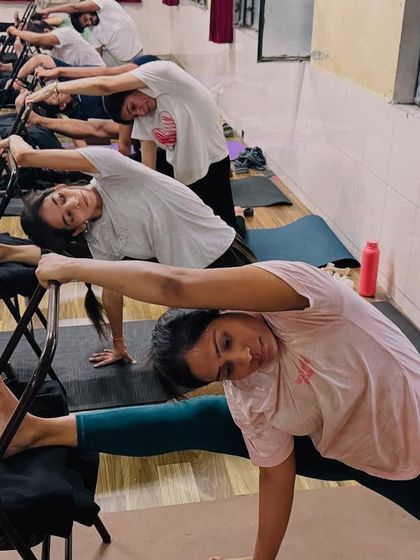 Using chairs, my students practice a deep side stretch. The chair supports their leg, allowing them to focus on opening the side of their body.