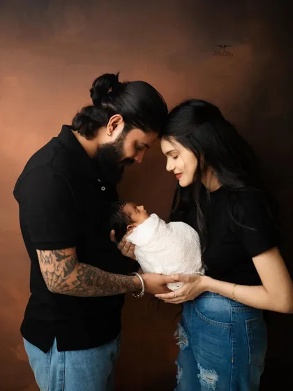 A modern and heartfelt newborn family portrait. The parents, dressed in black, create a beautiful frame as they hold their swaddled baby together.