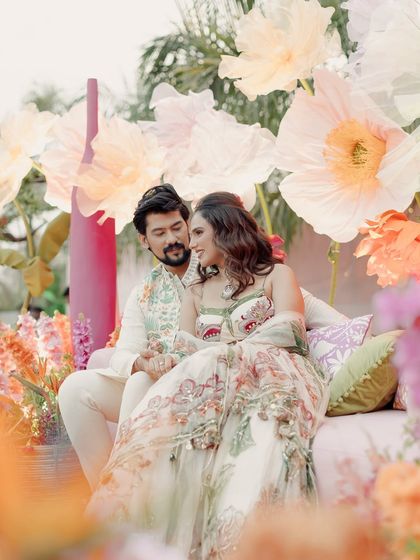 The beautiful couple surrounded by a stunning floral backdrop. Janvi's radiant makeup and soft waves fit perfectly with the romantic and whimsical atmosphere of her Mehndi.