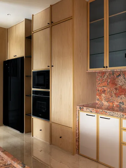 The kitchen in 'ARAH' features light wood cabinetry and a striking red-orange marble backsplash. The tall unit integrates the oven and microwave, creating a seamless and functional design.