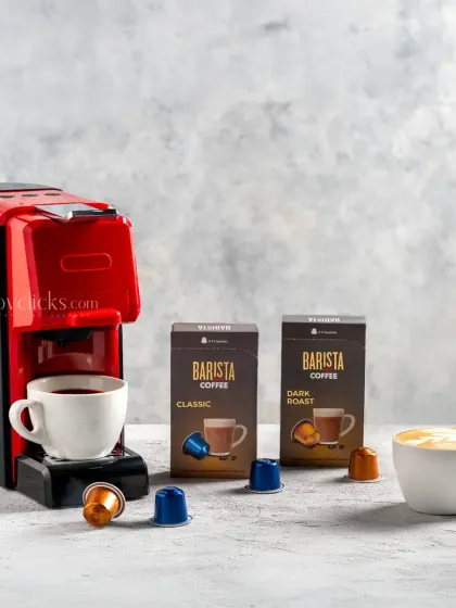 A product shot of a Barista coffee machine with its branded coffee pods and a freshly made cappuccino.