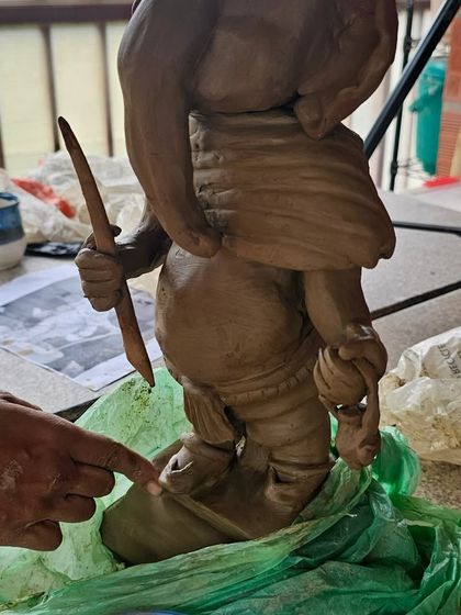A student uses a wooden tool to carve intricate details onto their Ganesha sculpture.