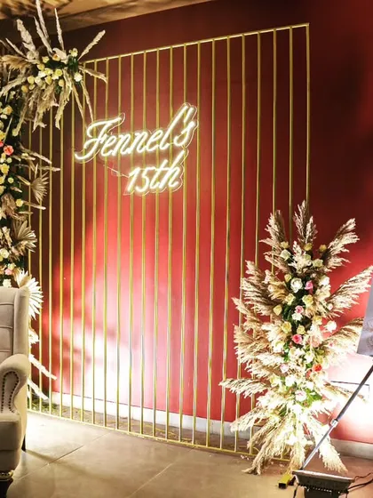 A stylish photo corner at the anniversary event, featuring a neon sign, a comfortable wingback chair, and floral arrangements. We design these spaces to encourage guest interaction and create lasting memories.