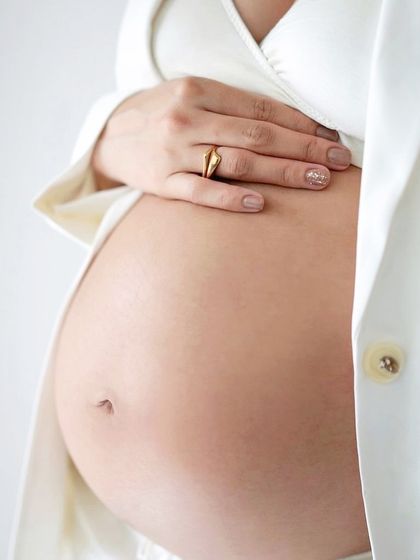 A detail shot of a bare baby bump, framed by a stylish white blazer.