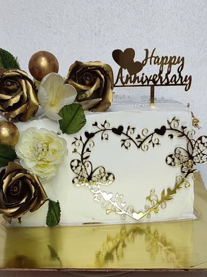 A rectangular anniversary cake with a beautiful heart-shaped topper and golden roses.