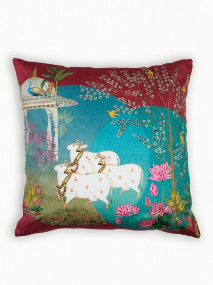 Another design from our Pichwai collection, this cushion depicts a serene pastoral scene with cows and lotuses. The deep maroon and teal color palette adds a touch of regal splendor to the traditional artwork.