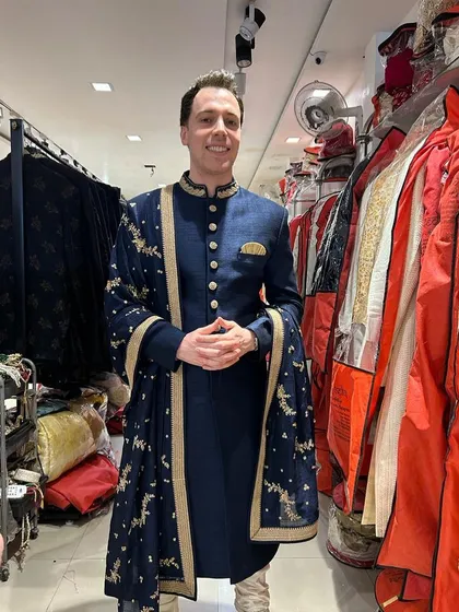 A happy client looking sharp in our navy blue sherwani with a gold embroidered dupatta. This classic combination is perfect for any wedding event.