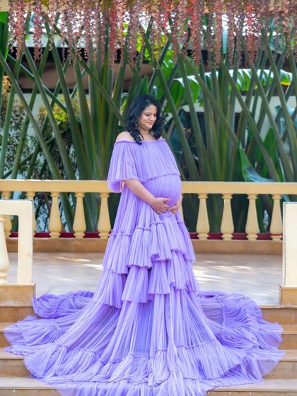 A beautiful portrait of a mom-to-be in a lavender gown, standing on a veranda with hanging flowers.