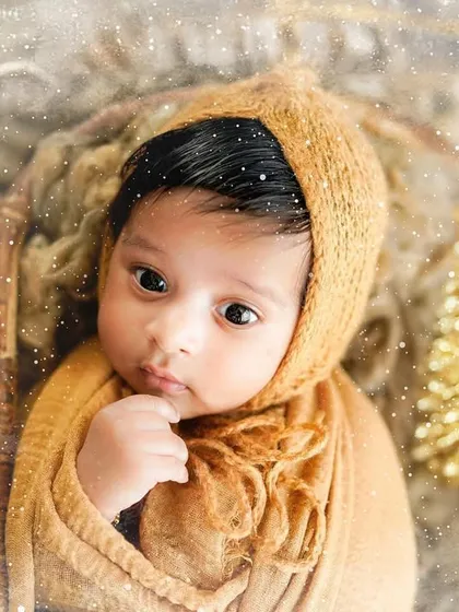 A close-up of a newborn's curious gaze amidst golden Christmas decorations. We focus on capturing these quiet, beautiful moments during our holiday sessions.