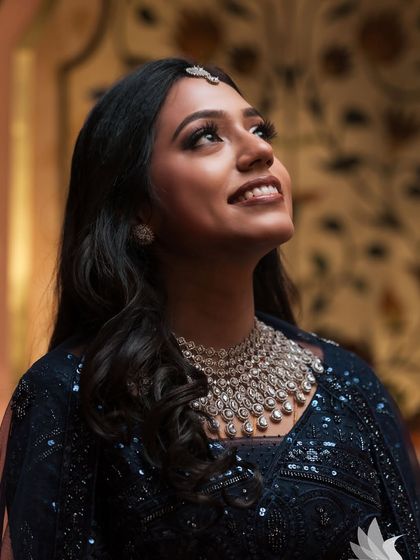 An artistic portrait of Dr. Akshara looking up. The soft lighting beautifully illuminates her face, showcasing the glamorous reception makeup.
