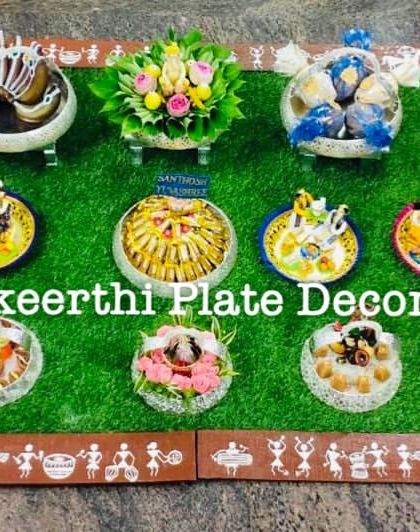 A grand engagement setup with German silver plates and a Warli art border on the carpet. The display includes a mix of traditional dolls and modern gift arrangements.