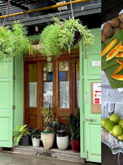 A green-painted cafe front with hanging plants, next to a vendor selling green jujubes and sliced mango.