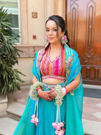 A bride ready for her Mehendi ceremony with her hair in a textured ponytail, adorned with floral jewelry. This style is practical for the event while still looking festive and beautiful.