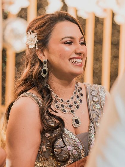 A close-up of the bride's happy face during the reception. The soft side-swept hair with a floral accessory adds a touch of romance to her glamorous look.
