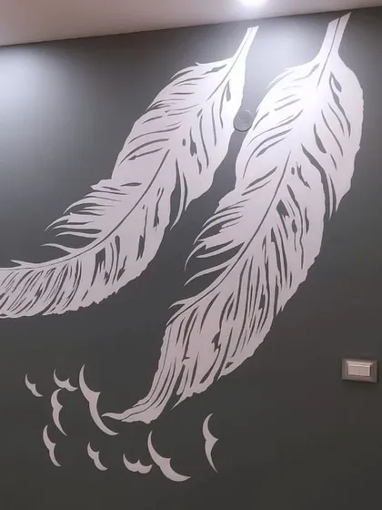 An elegant and minimalist stencil design featuring two large white feathers on a dark grey wall. This simple yet striking artwork is perfect for creating a serene and sophisticated focal point in any room.