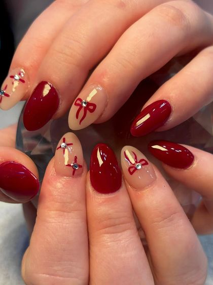 Another look at the festive red bow nails, showing the combination of solid red and sheer nude bases for a varied yet cohesive holiday manicure.