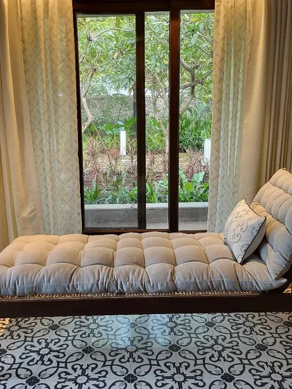 A comfortable chaise lounge I placed by the window in the Alibaug villa. The plush, tufted cushion and patterned floor create a perfect nook for reading and enjoying the garden view.