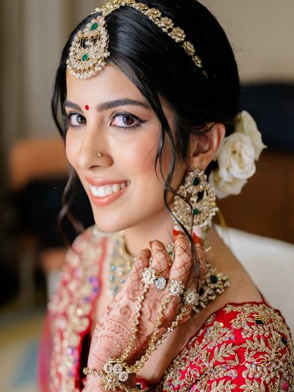 A close-up of a classic bridal look, featuring kohl-defined eyes, a traditional bindi, and flawless skin. The white flowers in her hair add a touch of softness to the regal ensemble.