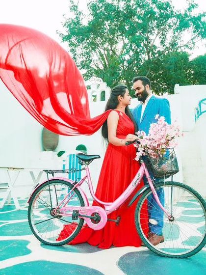 A playful and vibrant pre-wedding shoot in a Santorini-themed setting. The client's red flying gown adds a pop of color, perfectly complementing the fun, summery vibe.