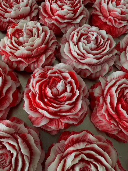 A stunning handcrafted peony candle with intricate red and white swirls, designed to look like a flower in full bloom.