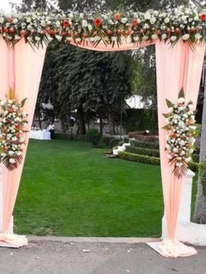 A simple entrance arch for an outdoor wedding. The arch is draped with peach-colored fabric and decorated with fresh flower bouquets.