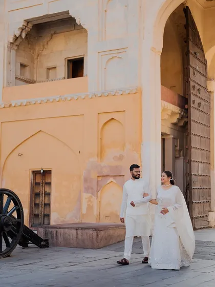 A candid walking shot of the couple at Amer Fort, capturing a natural interaction against the historic stone walls and grand wooden doors.