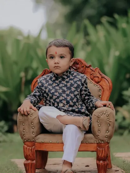 A full view of the handsome little boy in his floral-patterned kurta, seated confidently. This posed shot highlights the beautiful details of his outfit and his calm demeanor.