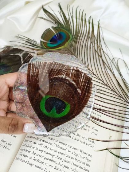 This coaster was made by preserving a real peacock feather in clear resin with silver flakes. It’s a unique way to bring the beauty of nature indoors.