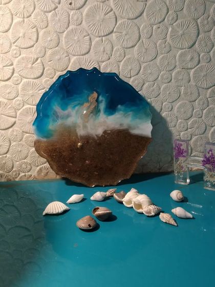 This beach-themed resin coaster is a perfect miniature ocean scene. It features deep blue water, lacy white waves, and a sandy shore, displayed here with real seashells.